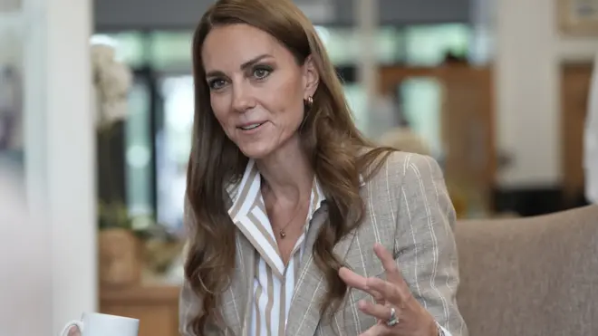 Księżna Walii Catherine na zdjęciu siedząca na sofie, w trakcie mówienia. Ma rozpuszczone włosy i złote kolczyki