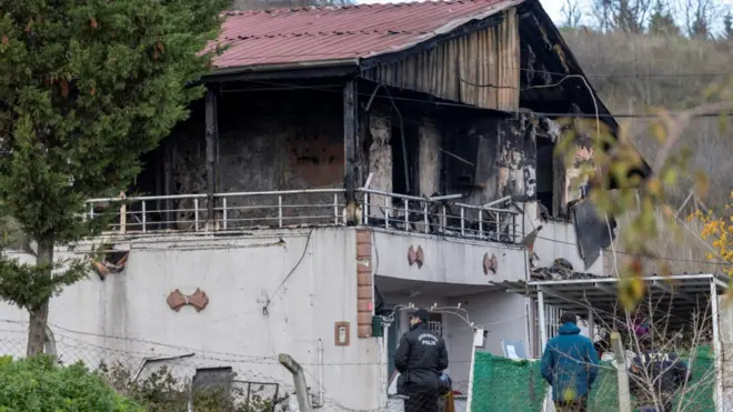 Kırmızı çatılı iki katlı evin balkon katının ciddi şekilde yandığı görülüyor. Evin çevresinde iki polis var.
