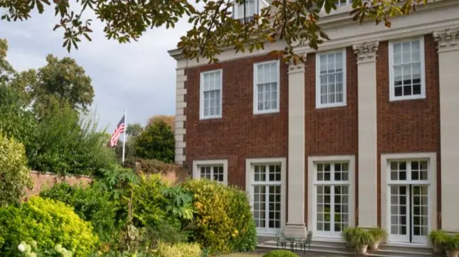 Stone paved path leading from Winfield House, a red brick building, with a US flag flying next to it