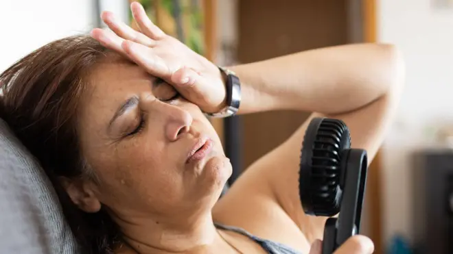 一名女子大汗淋漓,用手持電風扇為自己降溫