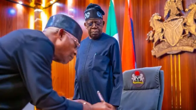 Vice Admiral Ibok-Ete Ibas (Rtd) signin on paper while President Bola Tinubu watches