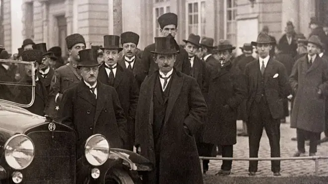 İsmet İnönü ve diğer delegeler bir otomobil önünde kameraya poz veriyor. Üzerlerinde takım elbise, palto ve uzun şapkalar var.