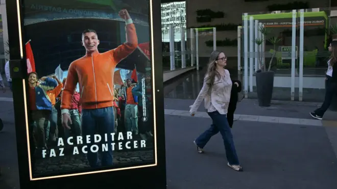 Propaganda de site de apostas em painel em rua de São Paulo, com transeunte passando ao fundo