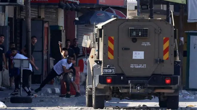 فلسطينيون يلقون حجارة على مركبة عسكرية إسرائيلية خلال غارة نفذها الجيش الإسرائيلي في مخيم الأمعري بالقرب من رام الله في 18 أغسطس/آب 2025