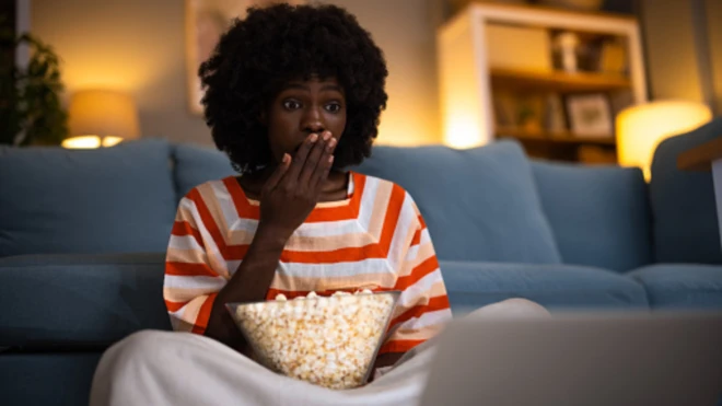 Black woman hold bowl of popcorn for hand dey watch movie