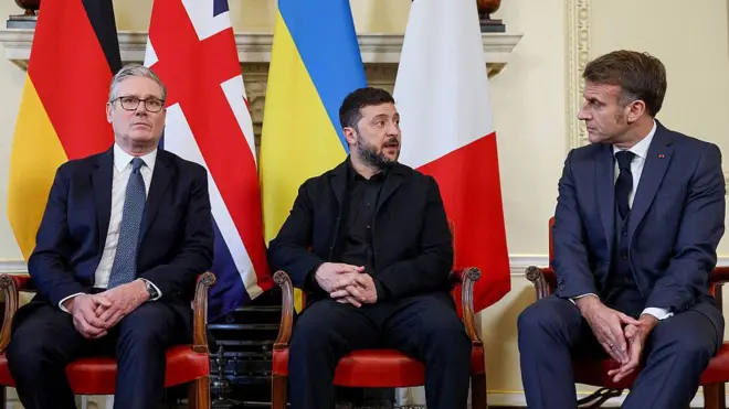 Стармер, Зеленский и Макрон сидят на стульях на фоне национальных флагов