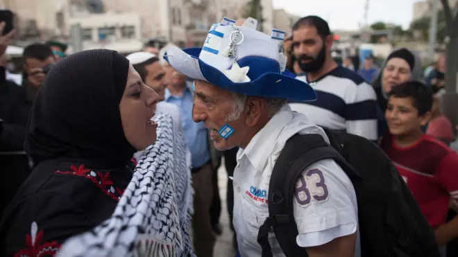 Uma mulher palestina usando um lenço na cabeça e um homem israelense usando um chapéu azul e branco com a bandeira israelense gritam um com o outropixbet nacional netJerusalém