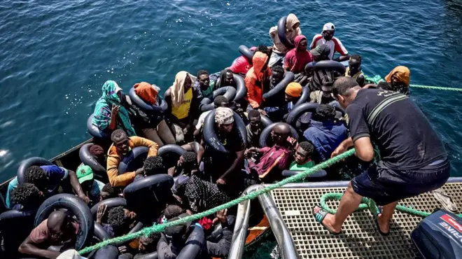 An illegal migrant vessel is tied on to the Tunisian coast guard patrol boat before its passengers are asked to disembark