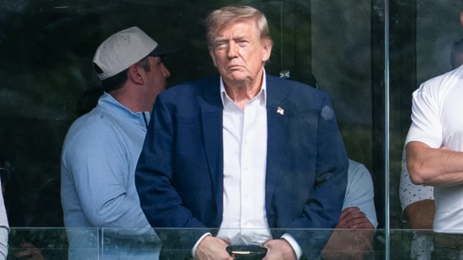 Trump elleri kemerinde bir şekilde uzaklara bakarak bir şeyler izliyor.
