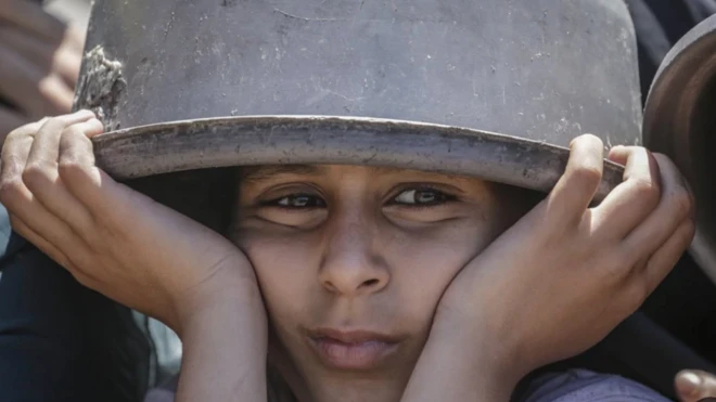 بچه‌ای قابلمه را روی سرش گذاشته و اندوهگین نگاه می‌کند