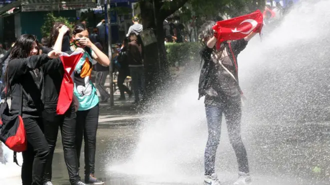 Polisin su püskürtüğü kadın protestoculardan biri elinde Türk bayrağıyla yüzünü kapatıyor, diğer üçü bir arada duruyor.