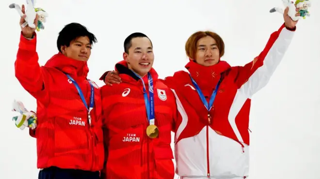 3人がメダルを首から下げ、肩を組んで笑顔で立っている。手には大会マスコットのぬいぐるみを持っている