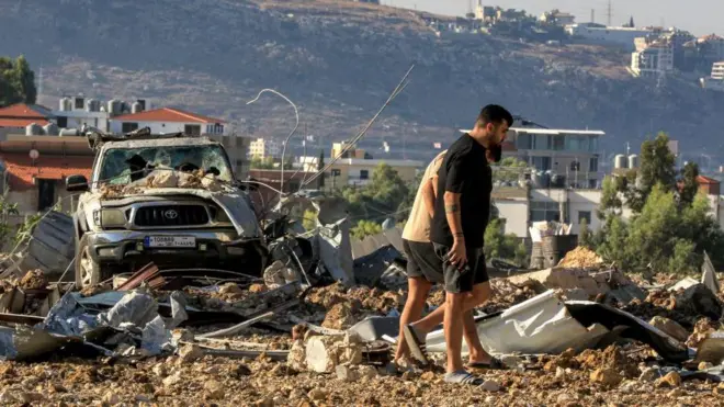 شخصان يتفقدان موقع غارة جوية إسرائيلية في الجية على طول الطريق السريع الذي يربط بيروت بمدينة صيدا الجنوبية، لا يظهر وجهاهما في الصورة التي التقطت نهاراً