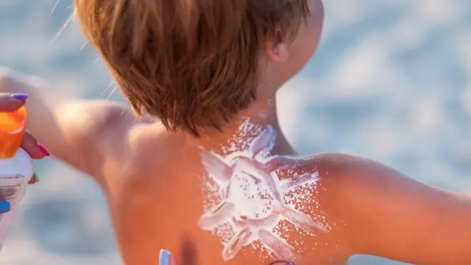 Mom applies sunscreen to the child's back and draws the sun on the beach