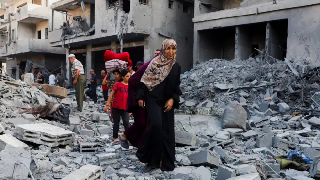 Люди на развалинах дома в Газе. На переднем плане женщина в черной одежде и цветном головном платке