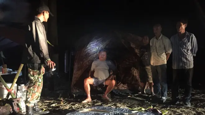 ภาพถ่ายนายเปรมชัย กรรณสูต (กลาง) ขณะที่ถูกเจ้าหน้าที่เขตรักษาพันธุ์สัตว์ป่าทุ่งใหญ่นเรศวรจับกุมตัว