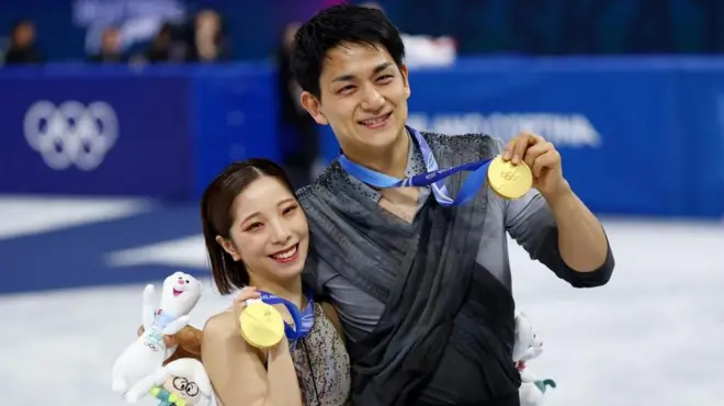 2人が体を寄せ、共に笑顔で、首から下げた金メダルを手で持ち上げている。