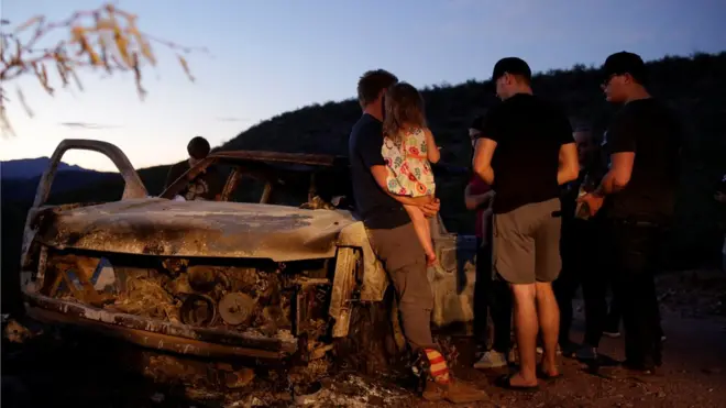 Relatives of the victims look at a burned-out vehicle in which four people were killed