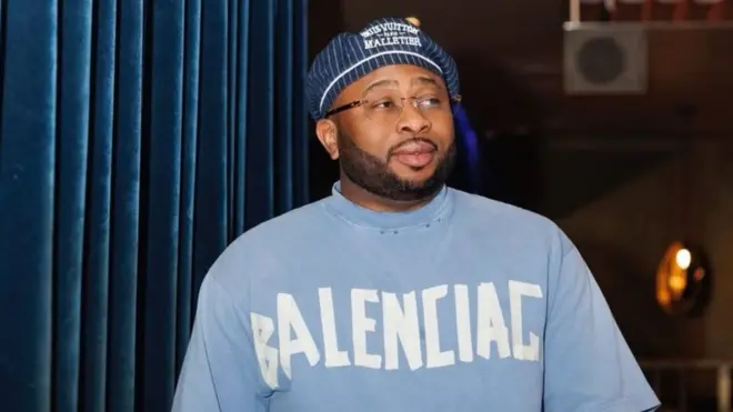 Olakunle Churchill wear one light blue t-shirt wit one blue cap