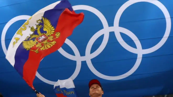 Болельщик с флагом России на фоне олимпийских колец