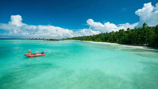 Barco chega ao litoral das ilhas Maldivas, em dia de sol, com um mar de água verde
