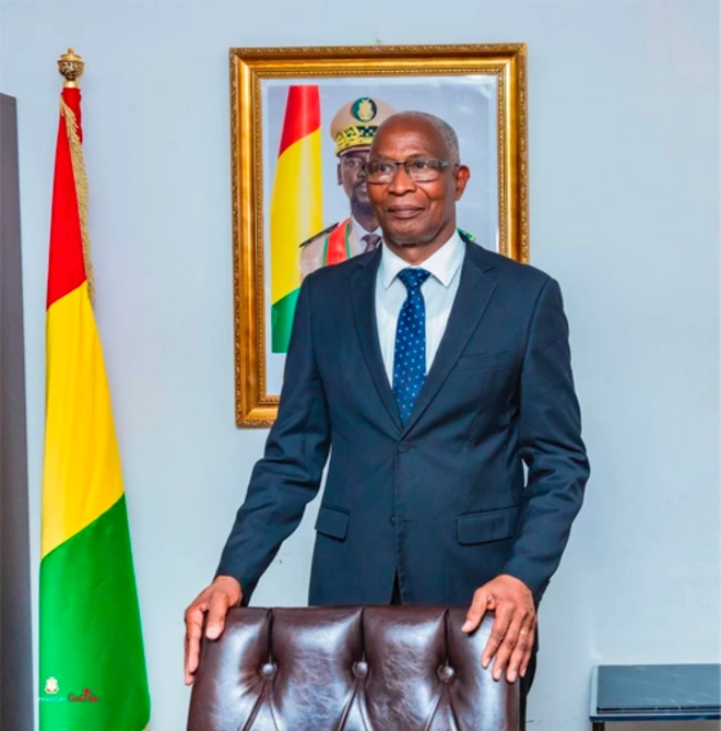 Amadou Oury Ba, Premier ministre de la Guinée debout avec à côté le drapeau de son pays et une image du chef de la junte derrière