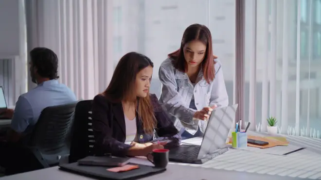 dos mujeres conversan en una oficina frente a un computador