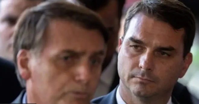Foto mostra Flávio Bolsonaro em segundo plano com o rosto de Jair Bolsonaro em primeiro plano desfocado