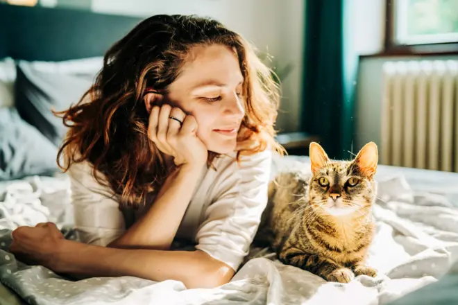 Bir kadın ve bir kedi yatağın üzerinde uzanmış halde