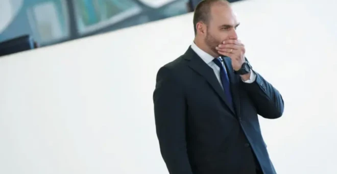 Foto mostra Eduardo Bolsonaro segurando a mão sobre a boca numa expressão que denota certa apreensão