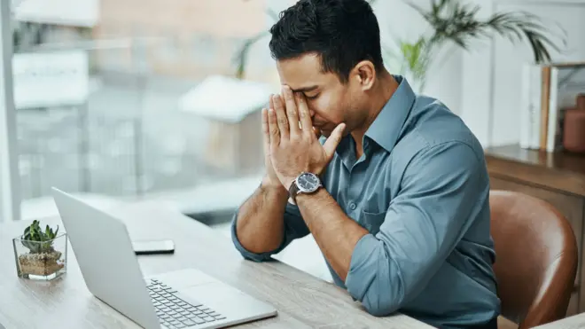 Homem com a mão no rosto preocupadoapp de apostas desportivasfrente a laptop