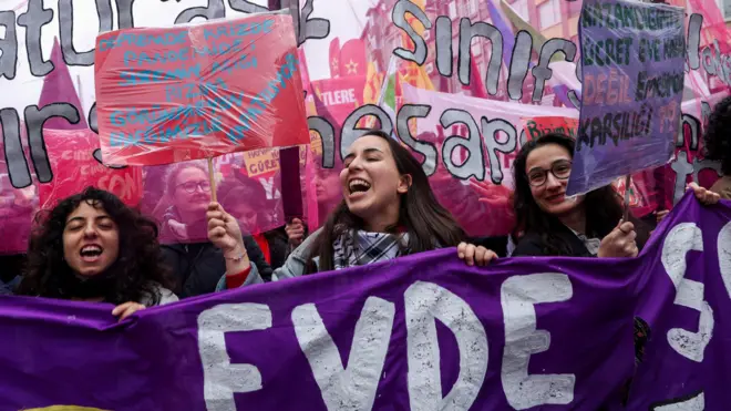 Kadın hakları gruplarının yürüyüşünden bir fotoğraf. Ellerinde pembe ve mor renkli döviz ve pankartlar taşıyorlar.