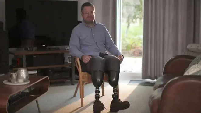 Ifoto yerekana umuntu yicaye ku ntebe mu bwicaro (salon). Afise amaguru y'amaterano, iruhande hari agatebe n'imeza. 