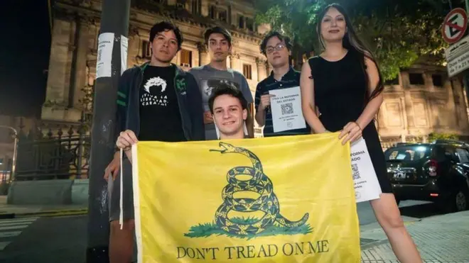 Jovens posando para foto à noite; um deles segurando uma Bandeiramon compte zebetGadsden