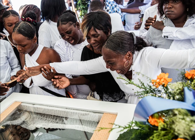 Mujeres lloran sobre un féretro que permite ver al difunto durante el funeral colectivo de ocho personas asesinadas en un ataque con drones en Puerto Príncipe, Haití, el 4 de octubre de 2025. Los drones que tenían como objetivo al presunto líder de una pandilla en un barrio de Puerto Príncipe controlado por estos grupos criminales terminaron matando a once civiles el 20 de septiembre de ese año.