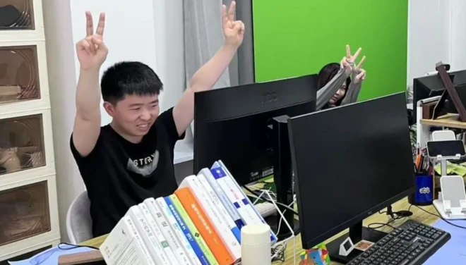 Shui Zhou ellerini zafer işareti yapacak gibi kaldırmış ve bilgisayar başında gülüyor.