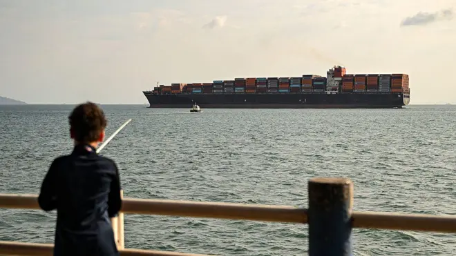 El buque portacontenedores Navios Constellation navega bajo bandera liberiana frente a un niño que pesca en Ciudad de Panamá.