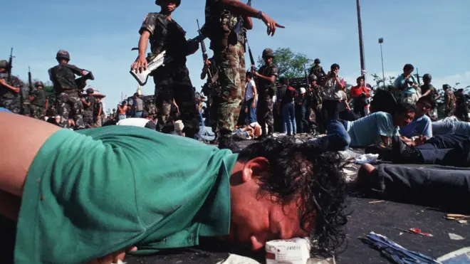 18 พ.ค. 2535 ชายคนหนึ่งใช้กล่องนมรองศีรษะไว้ขณะที่ถูกทหารถืออาวุธสั่งให้นอนคว่ำหน้าบนพื้นถนนอันร้อนระอุ