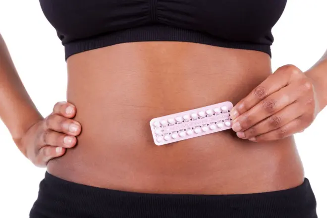 Femme noire tenant une tablette de pilules contraceptives contre son ventre