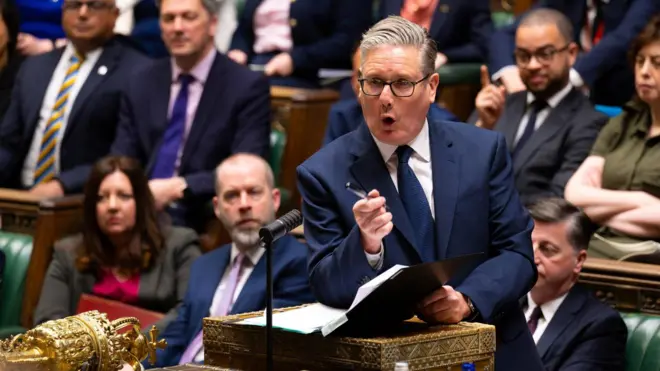 Keir Starmer de traje oscuro habla desde el atril en el Parlamento británico, con otros asistentes sentados en filas de fondo.