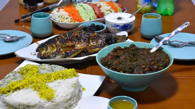 میز غذای ایرانی با سبزی‌پلو، قرمه‌سبزی، ماهی، سالاد و ماست