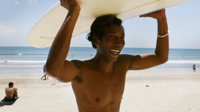 Seorang pemuda menyewakan papan selancar di Bali. Menurut survei, indeks kebahagiaan orang Bali sepanjang tahun ini lebih tinggi jika dibandingkan angka rata-rata kebahagiaan orang Indonesia.