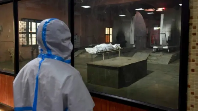 Relatives of a person who died of Covid-19 looking at the last rites being performed before cremation at Nigambodh Ghat crematorium