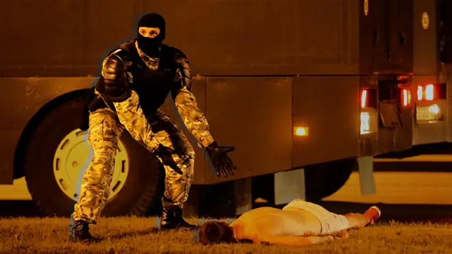 A special forces officer in Belarus stands next to a protester, who is lying face down on the ground