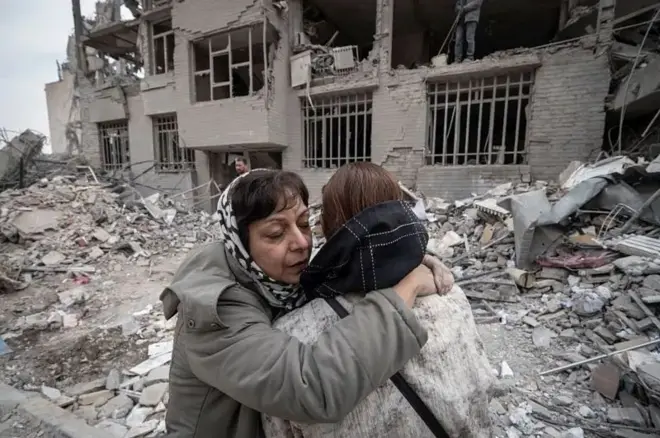 دوې مېرمنې د نړېدلې ودانۍ مخې ته ورغاړه وتلې دي