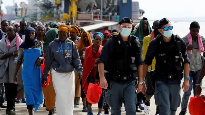 Мигранты в сопровождении полицейских сходят с борта судна