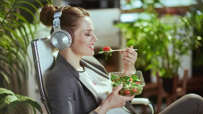 Una mujer con audífonos sentada comiendo una ensalada