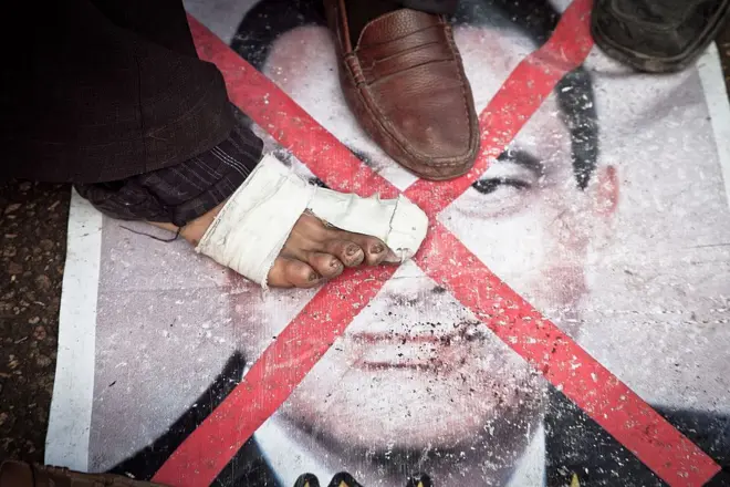 قاهره، مصر - ۶ فوریه ۲۰۱۱: یکی از معترضان ضد مبارک در میدان تحریر قاهره بر روی پوستر حسنی مبارک قدم می‌گذارد.
