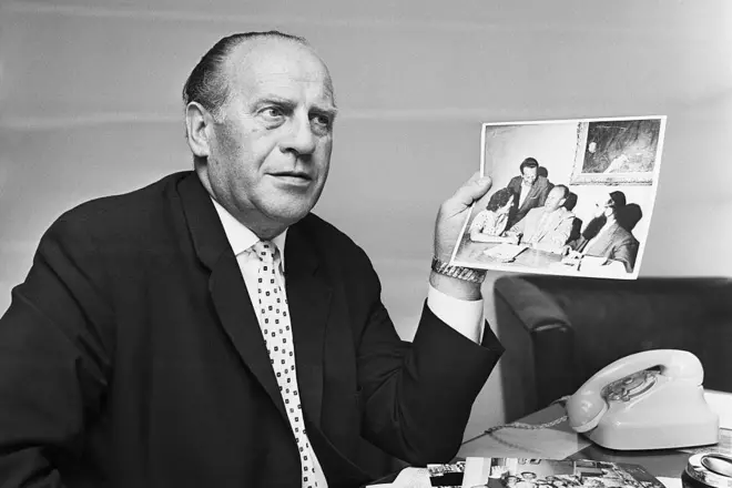 Foto em preto e branco mostra Oskar Schindler segurando uma foto do Holocausto