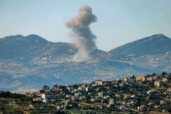 تصاعد الدخان عقب قصف إسرائيلي في جنوب لبنان، كما يُرى من موقع عبر الحدود في الجليل الأعلى شمال إسرائيل. 
يظهر في الصورة عدد من المساكن وأشجار في الصورة التي التقطت نهاراً.